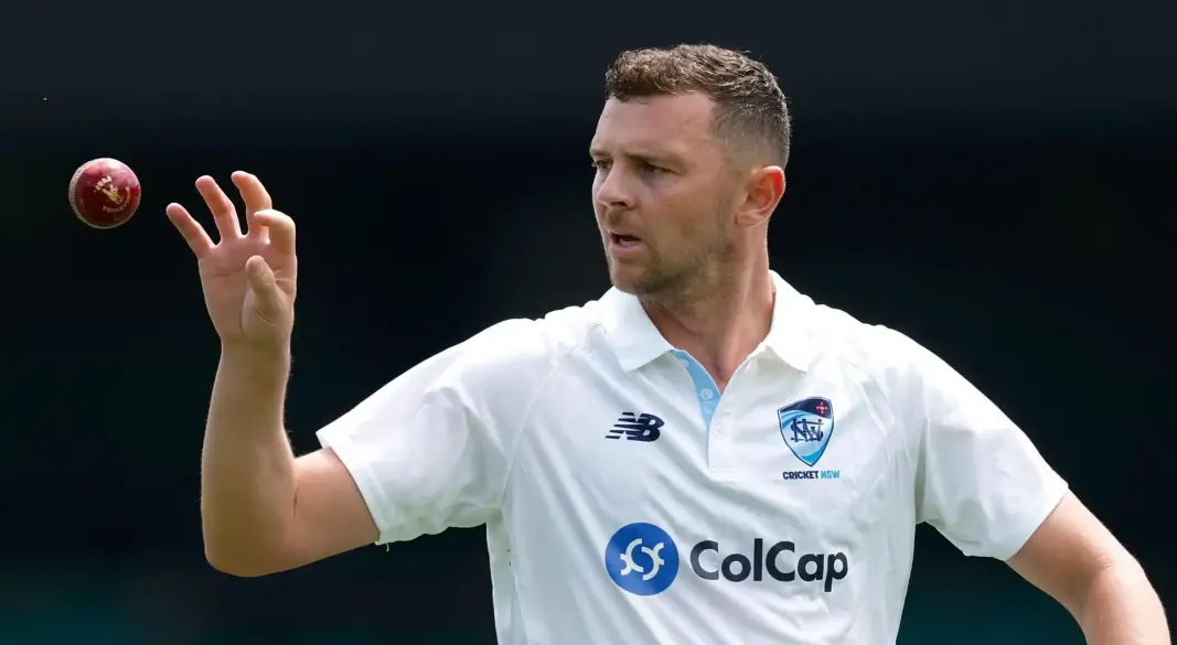 Cricket ball resting near stumps on an empty pitch under cloudy sky
